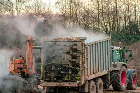 Excavator loads manure, hovering in the cold air, into a trailer Stock Photos