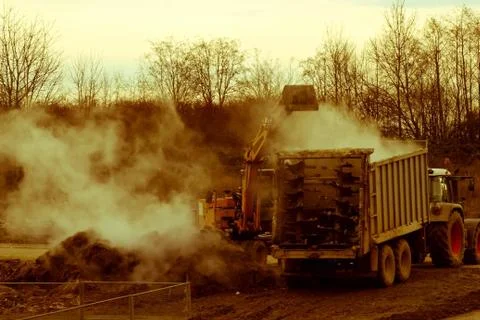 Excavator loads manure, hovering in the cold air, into a trailer Stock Photos