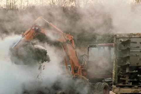 Excavator loads manure, hovering in the cold air, into a trailer Stock Photos