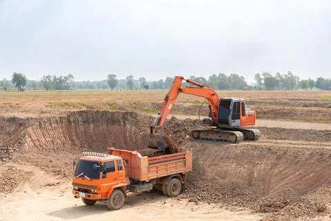 A excavator loads soil into the back of a dump truck. Stock Photos