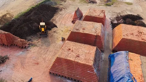 Excavator moving soil beside large stacks of red clay bricks at a brick works Stock Footage 340607699