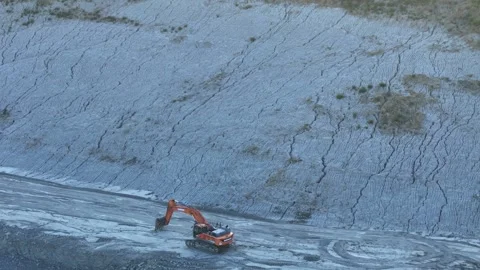 Excavator operating at quarry base beside exposed rock face with layered Stock Footage 346361674
