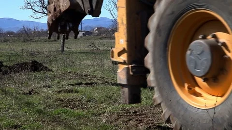 Excavator passing by and excavator digging a hole in a field Stock Footage 73449398