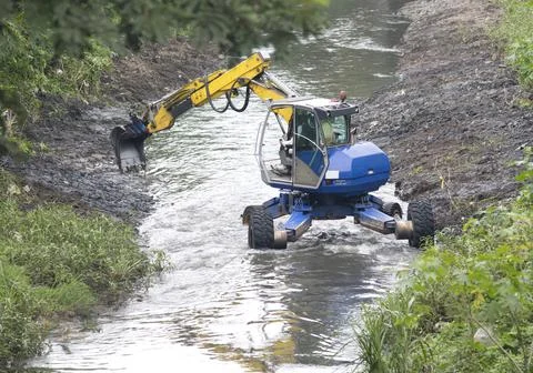 Excavator performing river dredging and clearing up the river banks. Stock Photos