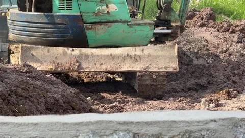 An excavator relocates soil across a construction site near a concrete boundary 库存影片 333632797