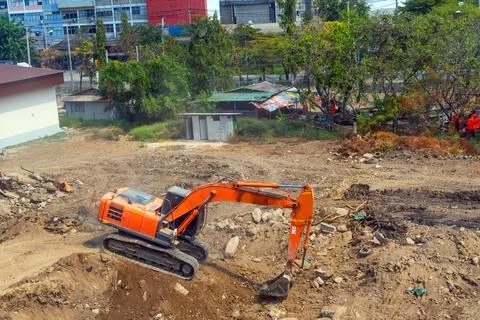 Excavator at work on construction site, thickets and other old houses around Stock Photos