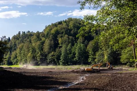 Excavators deepen clean drained Trakoscan reservoir basin by forested hills.. 写真素材