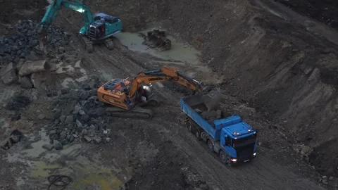 Excavators loading dump truck on muddy site at dusk Stock Footage 334549456