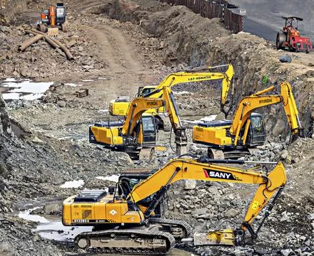 Excavators of various companies digging simultaneously for road widening work Stock Photos