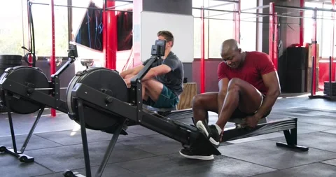 Exchanging smiles and sitting on rowing machines, diverse male friends rowing Stock Footage 336366808