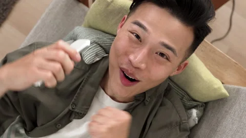 Excited asian guy lying on the sofa Video stock 227098314