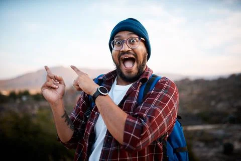 An excited backpacker points to the mountain view behind him on hiking trip Stock Photos