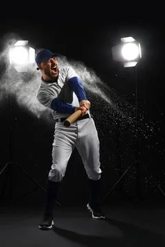 Excited baseball player hitting bat with powder explosion, studio lighting, s Stock Photos