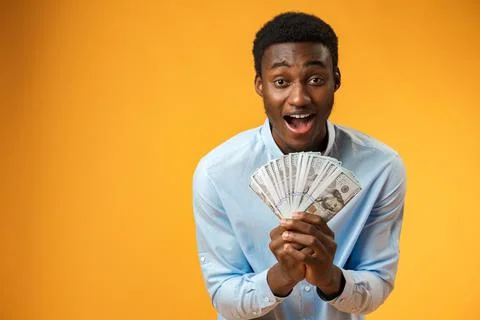 Excited black guy holding stack of Dollars in yellow studio 스톡 사진