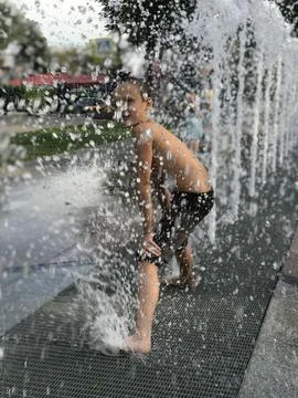 Excited boy having fun between water splashes, in fountain. Summer in the city Stock Photos