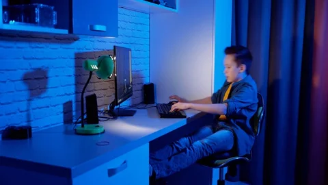 Excited boy playing games on a computer at home. Teen gamer sitting at the table Stock Footage 129164593