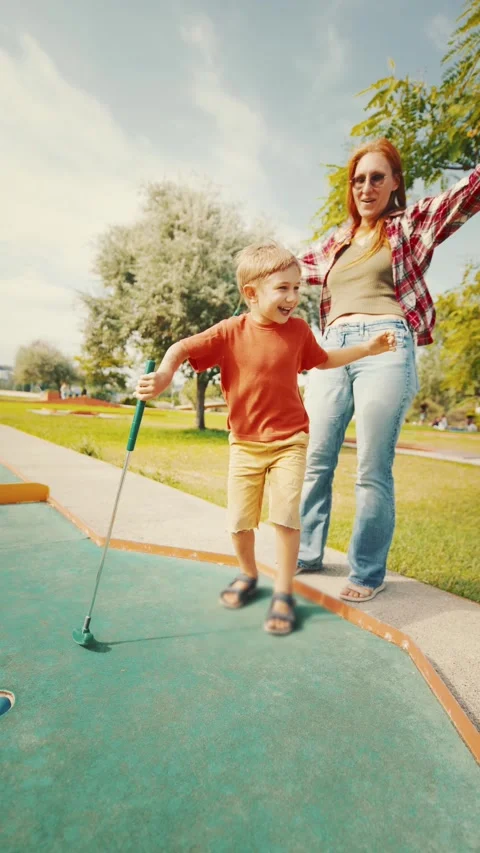 Excited child plays mini golf in sunny park with family on a warm afternoon Stock Footage 339461733