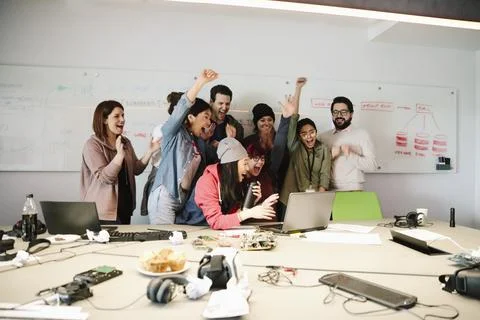 Excited computer programmers cheering at laptop in conference room meeting Foto stock