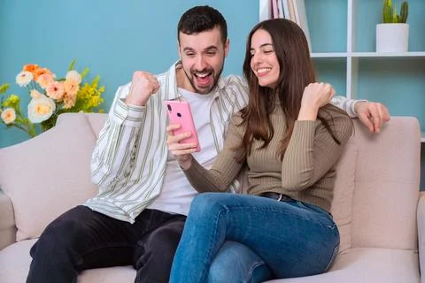 Excited couple celebrating while looking at a smartphone on the sofa. Stock-Fotos