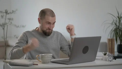 Excited Freelancer with beard in a gray jacket reading good news on a laptop. Video stock 128498156