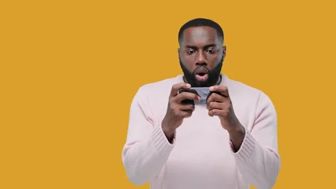 Excited guy playing games on mobile phone on yellow background Stock Footage 142579952