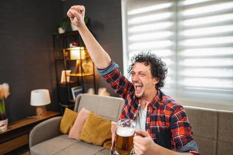 Excited man celebrating with beer while watching sports on tv at home Stock Photos