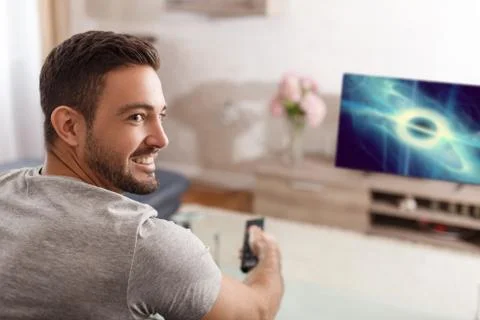 Excited man switch TV to sci-fi movie by remote control Stock Photos