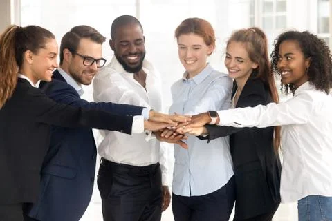 Excited multiethnic employees stack hands showing support and unity 库存照片