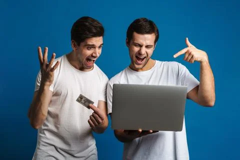 Excited two guys screaming while posing with laptop and credit card Foto stock