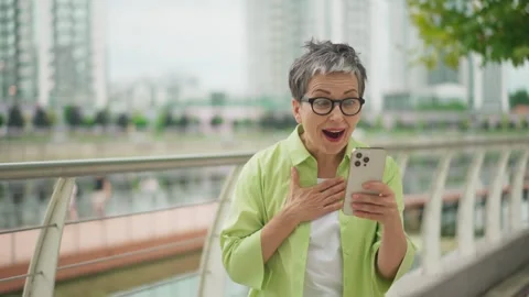 Excited woman celebrating something while holding smartphone outdoors. Smiling Stock Footage 311813252
