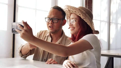 Excited young Asian couple is using smartphone to do video call with friend.. Stock Footage 338433267