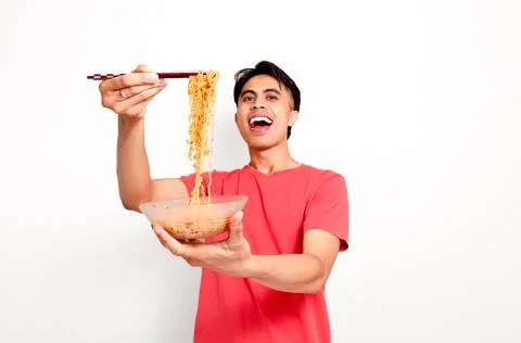 Excited young Asian man holding a bowl of noodles and lifting them with cho.. Stock Photos
