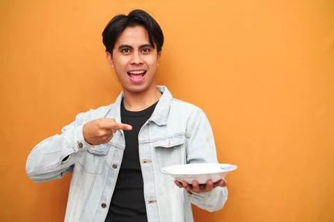 Excited young asian man with hungry face carrying empty plate with workspac.. Stock Photos