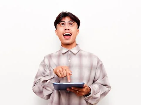Excited young Asian man using a digital tablet and looking up with a happy .. Stock Photos