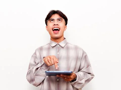 Excited young Asian man using digital tablet and looking up with happy expr.. Stock Photos
