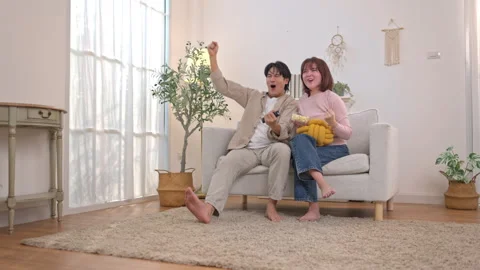 Excited young couple cheering on sofa while watching television Video stock 338427542