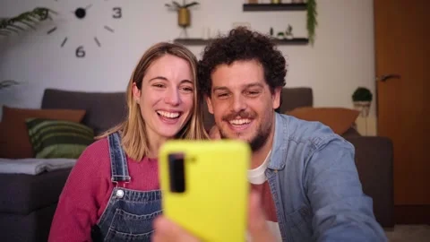 Excited young couple using phone hugging in living room at home for video call Stock Footage 258112197