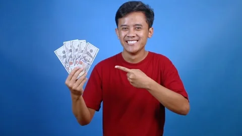 Excited young man pointing at a fan of dollar bills Stock Footage 327413745