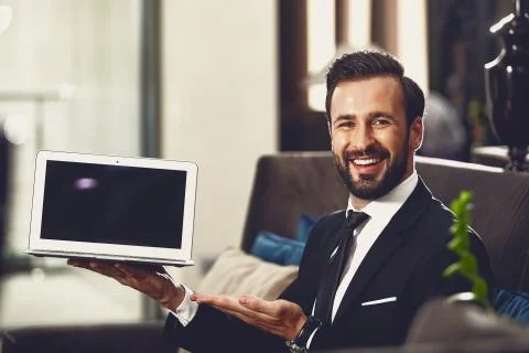 Excited young man smiling while demonstrating his laptop Stock Photos