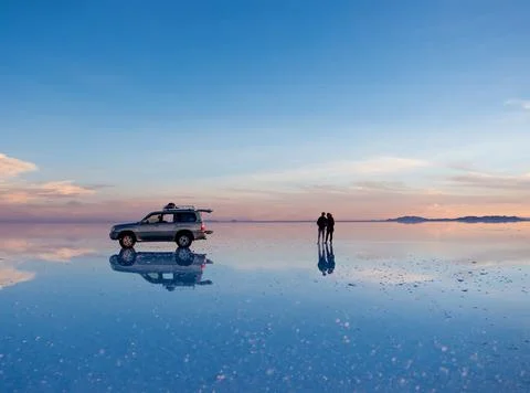 Exciting scenery of spacious Salar de Uyuni with couple and car Stock Photos