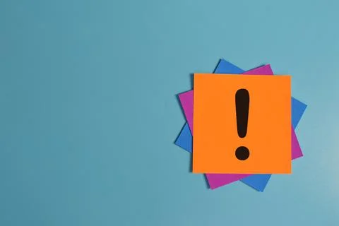 Exclamation mark drawn on memo note isolated on blue background. Copy space. Stock Photos