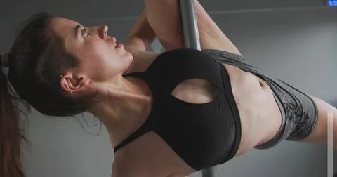 Executing inverted pole move athlete in sportswear gripping chrome pole in Stock Photos