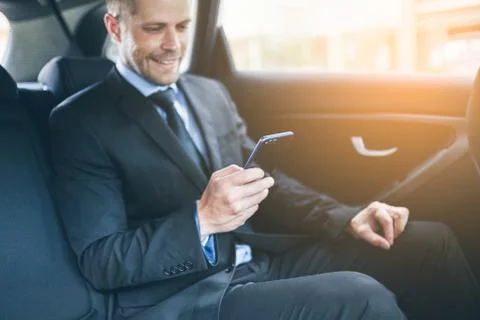Executive businessman at the back of car using a mobile phone Stock Photos