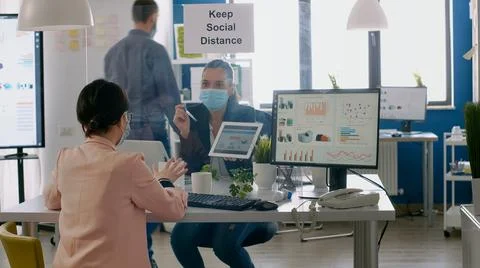 Executive manager with face mask showing statistics to her collegue 写真素材