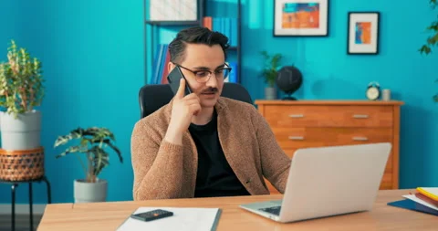 Executive sitting at desk in front of laptop holding cellphone having pleasant Stock Footage 163179776
