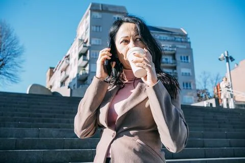 Executive woman having a coffee while talking on the mobile phone with her Stock Photos