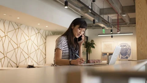 Executive writing down notes while using laptop and talking on phone in café Stock Footage 105614919