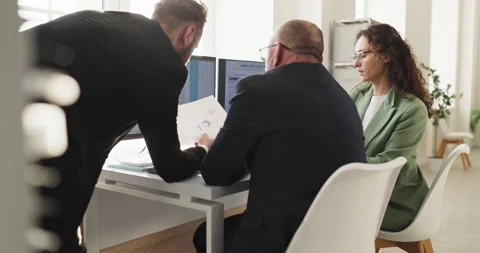 Executives and analyst discussing reports and data on monitors in bright office Stock Footage 330856904