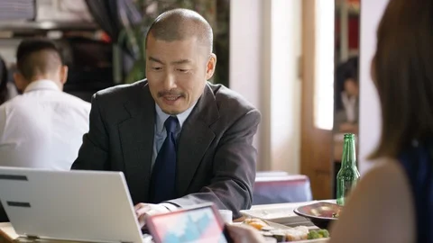 Executives using laptop and tablet, talking to each other in restaurant Video stock 107994048