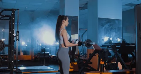 Exercise for biceps with a w-shaped barbell. Sports Hall. Dark, smoke, gym Stock Footage 98958260